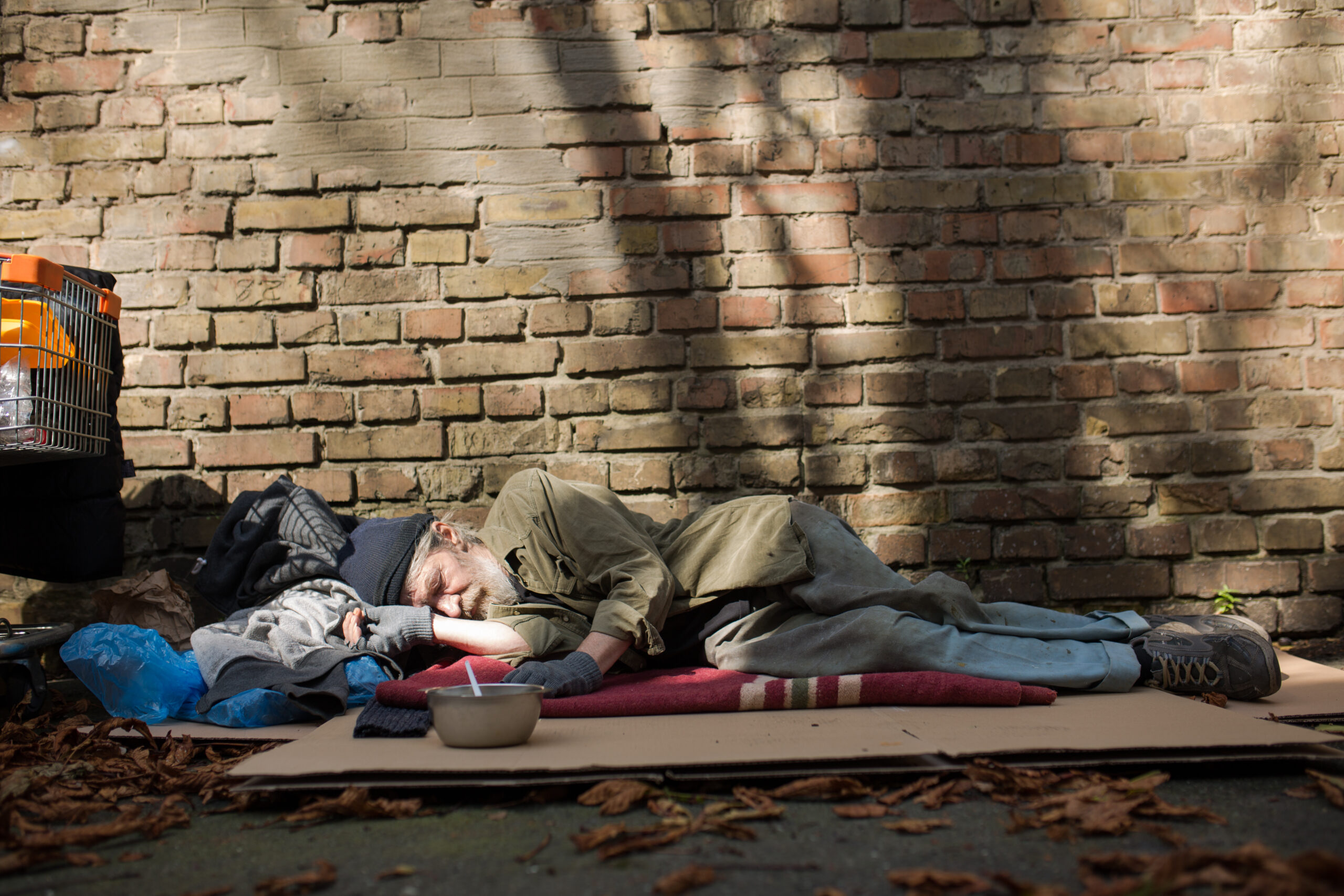 View of homeless man sleeping on cardboard on the ground.