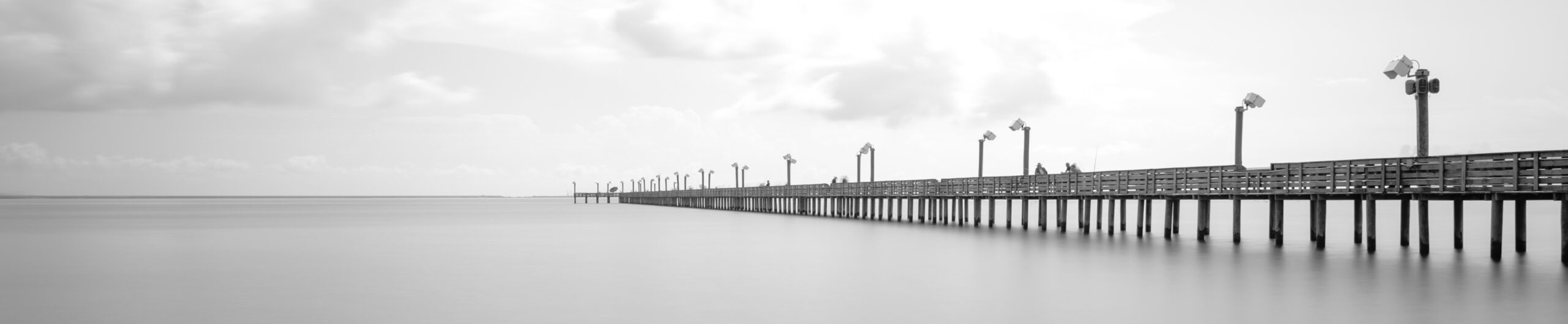 Long exposure wooden fishing pier stretching out over Galveston Bay in La Porte, Texas, USA. Foot pier for saltwater fishing with motion blurred people, recreation concept. Panorama nature seascape