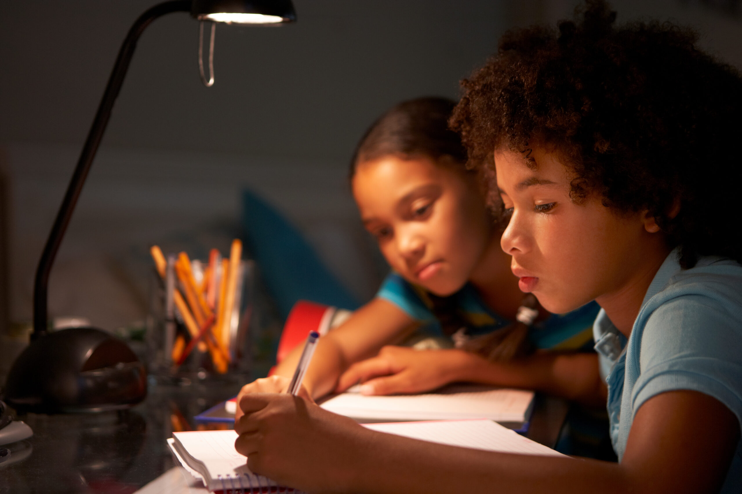 Two Children Studying At Desk In Bedroom In Evening