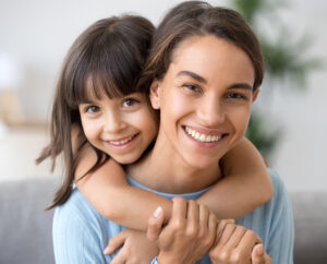 Happy mom and cute kid daughter embracing looking at camera